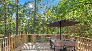 A wooden deck with a table and chairs, surrounded by a wooden railing, set in a forested area.