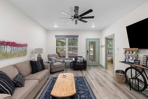 A modern living room with a sofa, armchairs, a coffee table, and a ceiling fan.