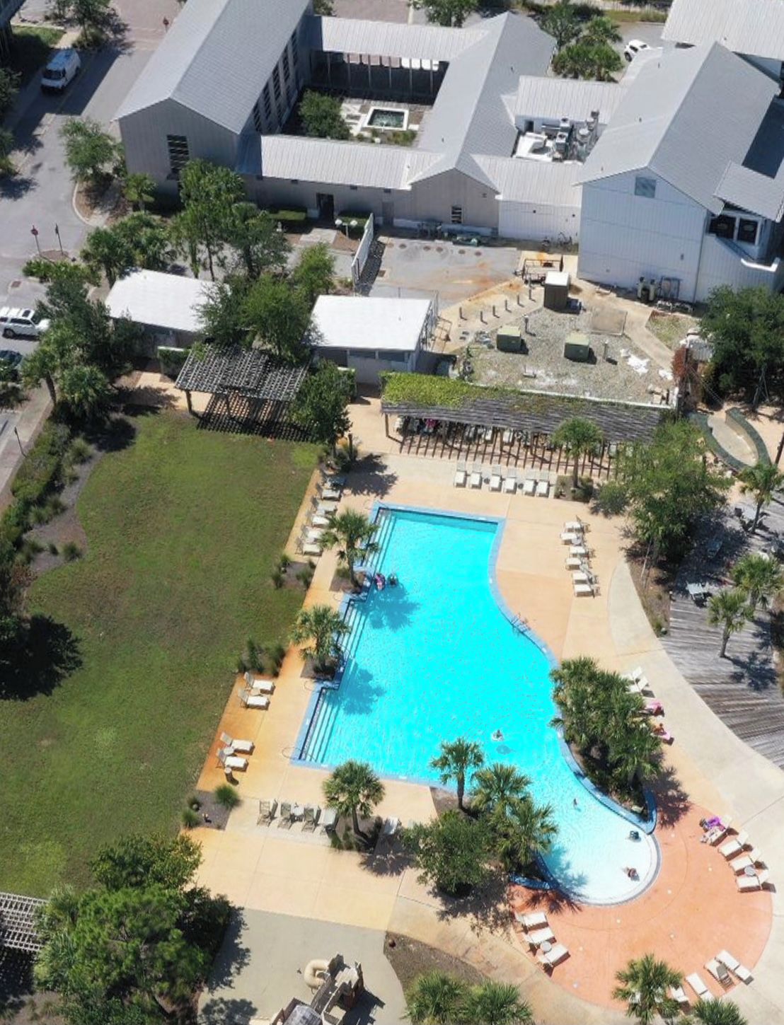 Vue aérienne d’un hôtel doté d’une grande piscine, entourée de chaises longues et de palmiers.