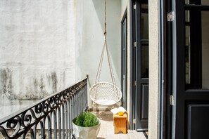 Ein Hängestuhl, ein kleiner Holzschemel und ein Blumentopf auf einem Balkon.