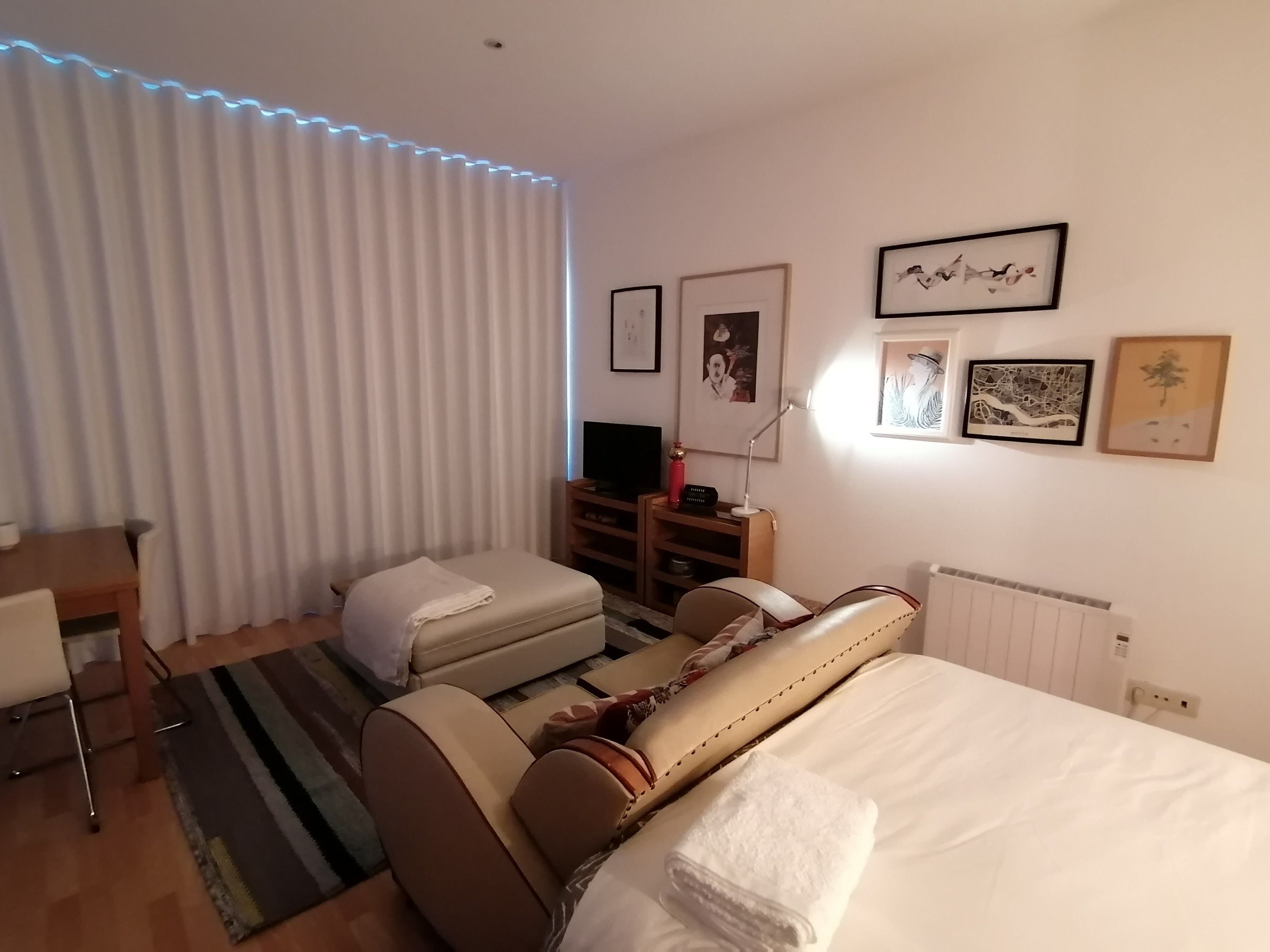A hotel room with a bed, a desk, a chair, a sofa, and a radiator.