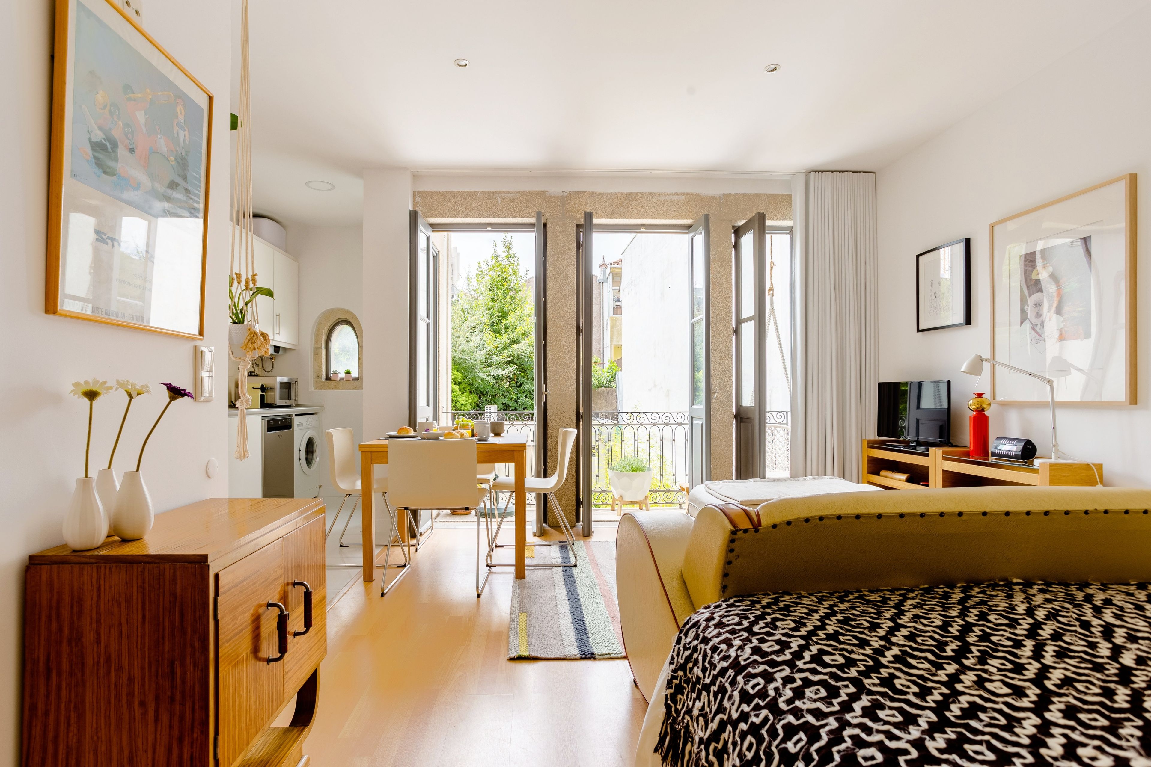A hotel room with a bed, a desk, a chair, a TV, and a balcony with a view of greenery.