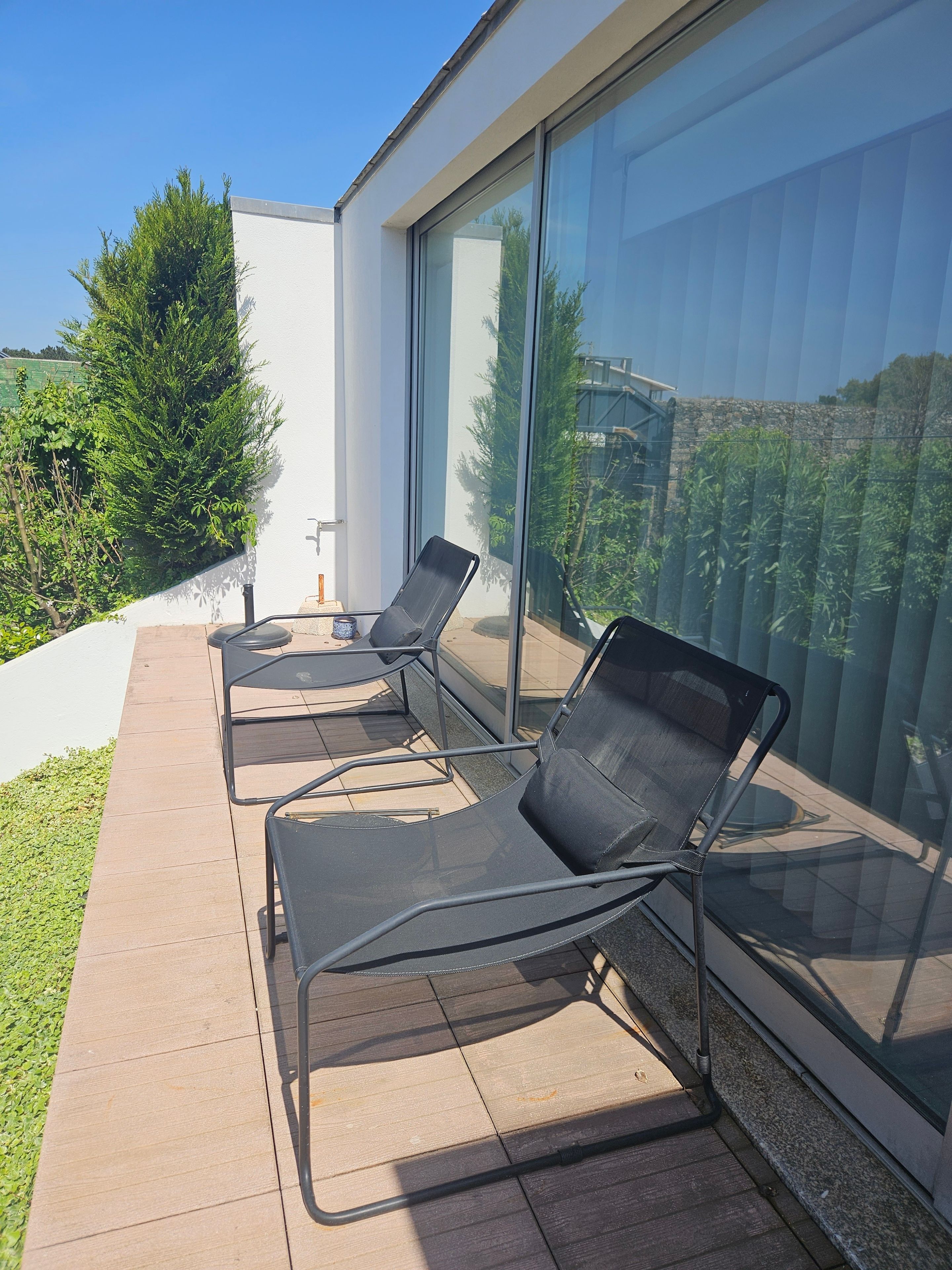 Un área de estar moderna al aire libre, con dos sillones y una mesa, contigua a un edificio con grandes ventanales.
