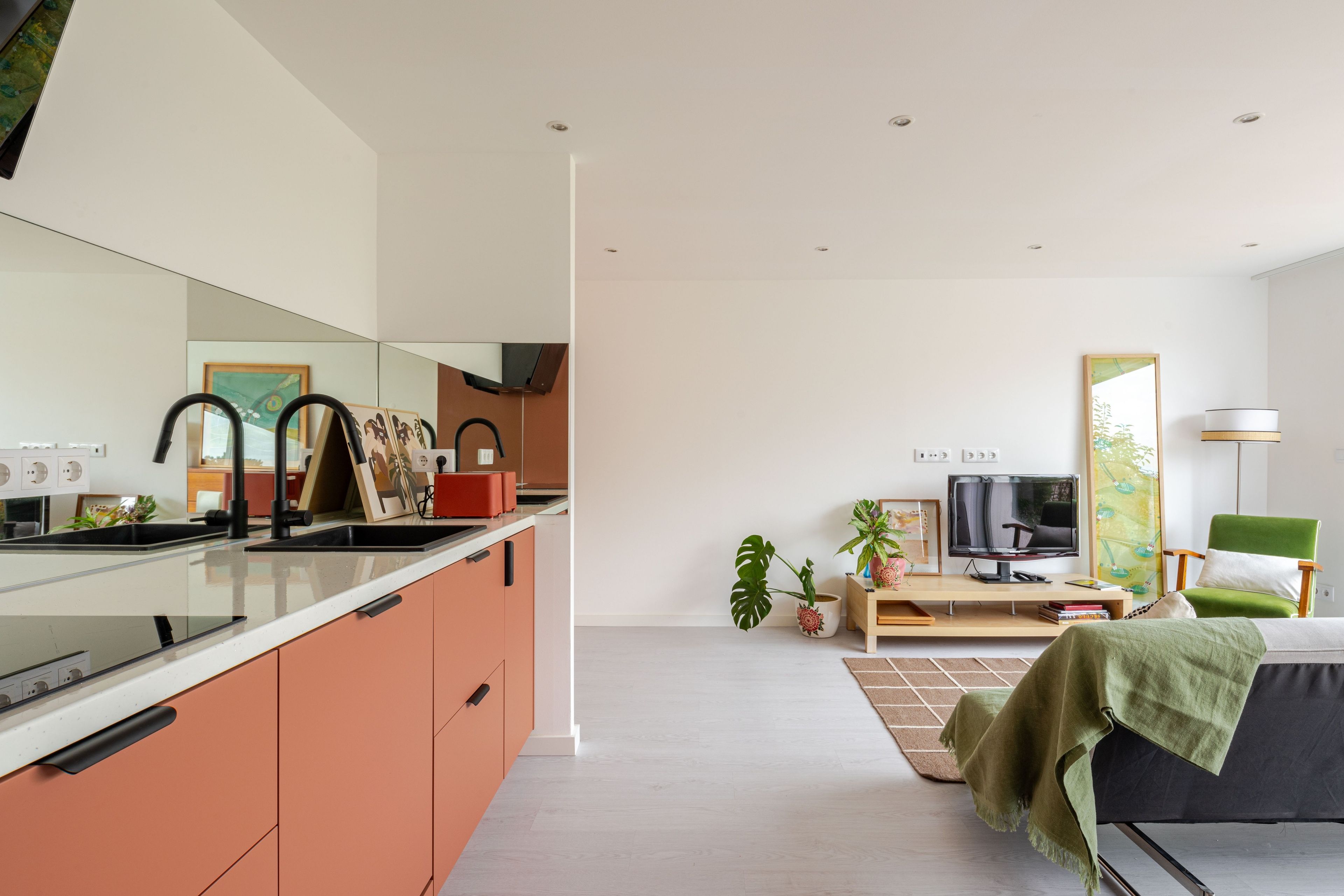 Eine moderne Küche mit einer großen Kochinsel, ein Essbereich mit Fernseher und Sitzgelegenheiten sowie ein Wohnzimmer mit Sofa und grünem Sessel.