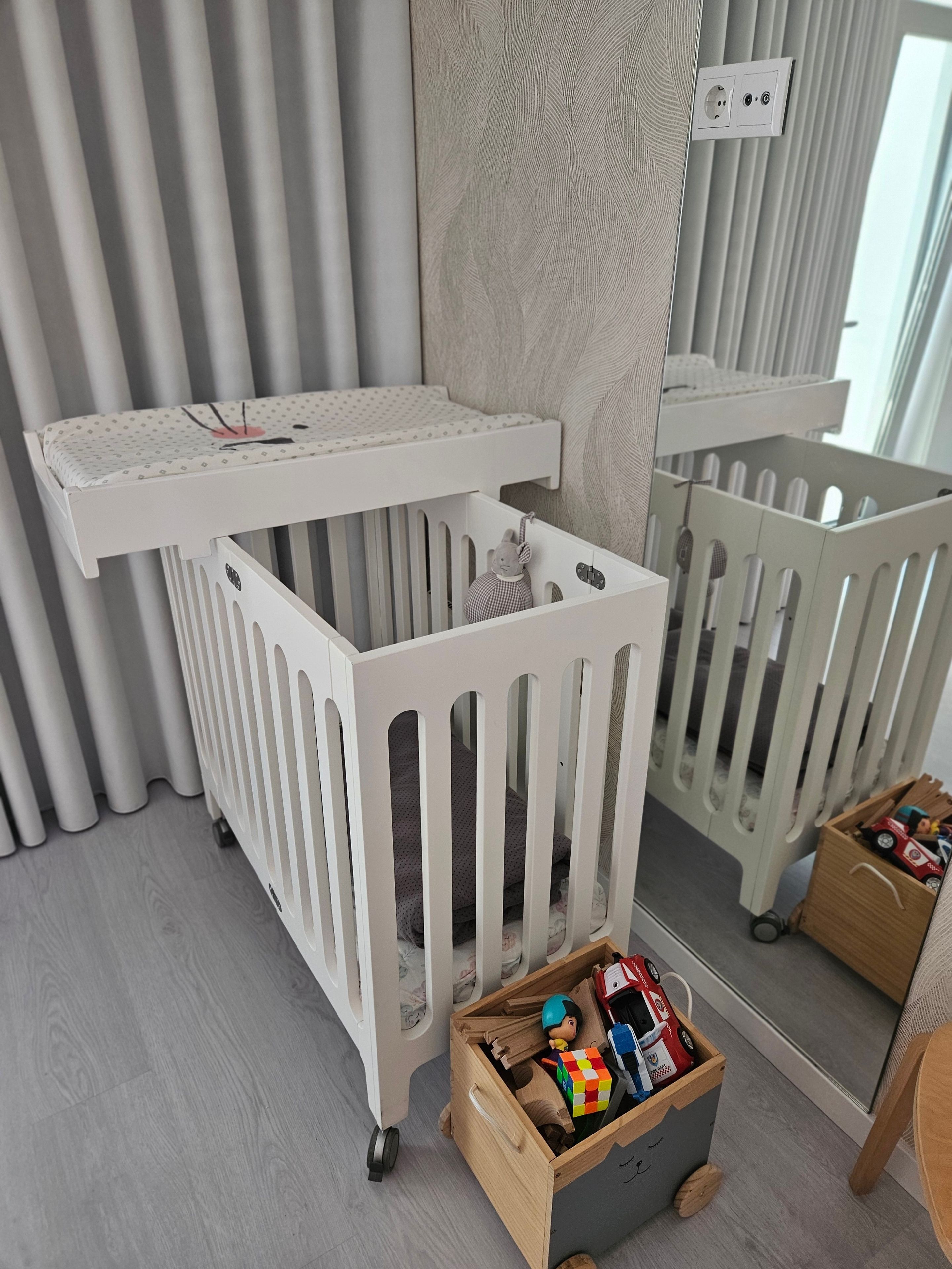 Ein weißes Babybett mit einer Aufbewahrungsbox und einem Spiegel.