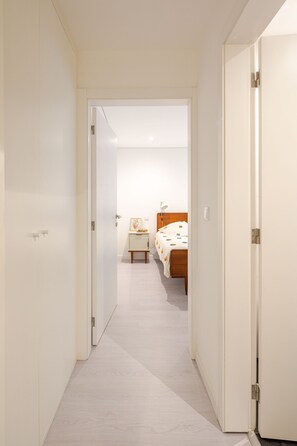 Un pasillo estrecho que conduce a un dormitorio con cama, mesita de noche y mesilla.