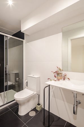 Un baño moderno con inodoro, cabina de ducha y lavabo con espejo.