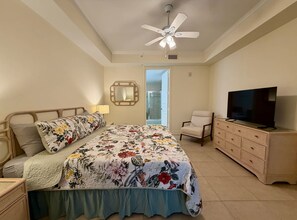 Een slaapkamer met een bed, een stoel, een televisietoestel, een dressoir en een plafondventilator.