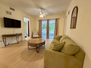 A living room with a flat-screen TV, a round coffee table, a sofa, a ceiling fan, and a view of the outdoors. - Gulfside Getaway - Free Bikes - 1 Mi to Beach (Bonita Springs)