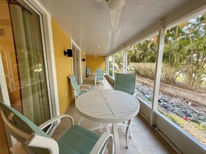 A covered patio with a round table and chairs, a ceiling fan, and a view of a garden with palm trees. - Gulfside Getaway - Free Bikes - 1 Mi to Beach (Bonita Springs)