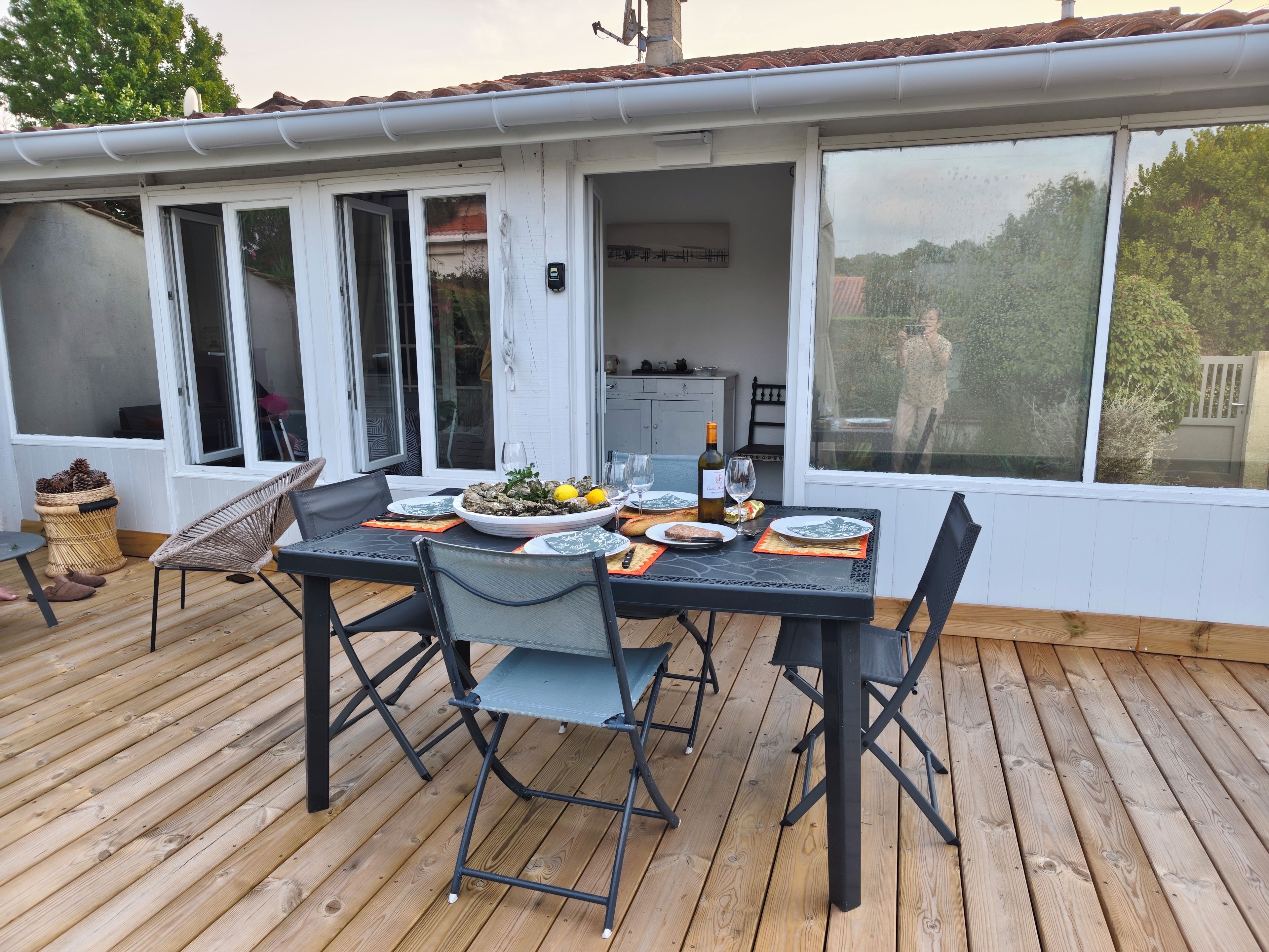 An outdoor dining area with a table set for two, surrounded by chairs, on a wooden deck.