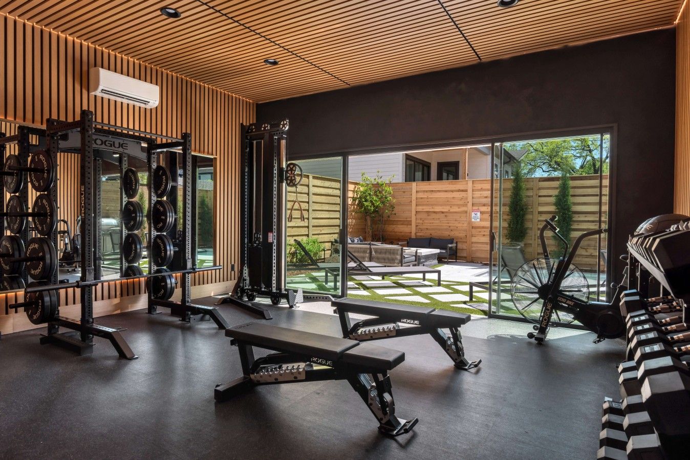 Un gimnasio con equipo de levantamiento de pesas, una banca y vistas al exterior.