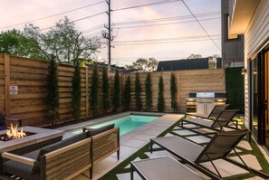 A backyard with a swimming pool, lounge chairs, a fire pit, and a wooden fence. - Sunny Modern Oasis • Pool, Hot Tub, Fire Pit, Grill, Rooftop (Nashville)