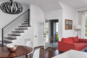 A modern living room with a staircase, a dining area, and a red sofa. - Sunny Modern Oasis • Pool, Hot Tub, Fire Pit, Grill, Rooftop (Nashville)