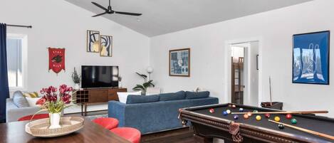 A living room with a pool table, a sofa, a television, and a ceiling fan.