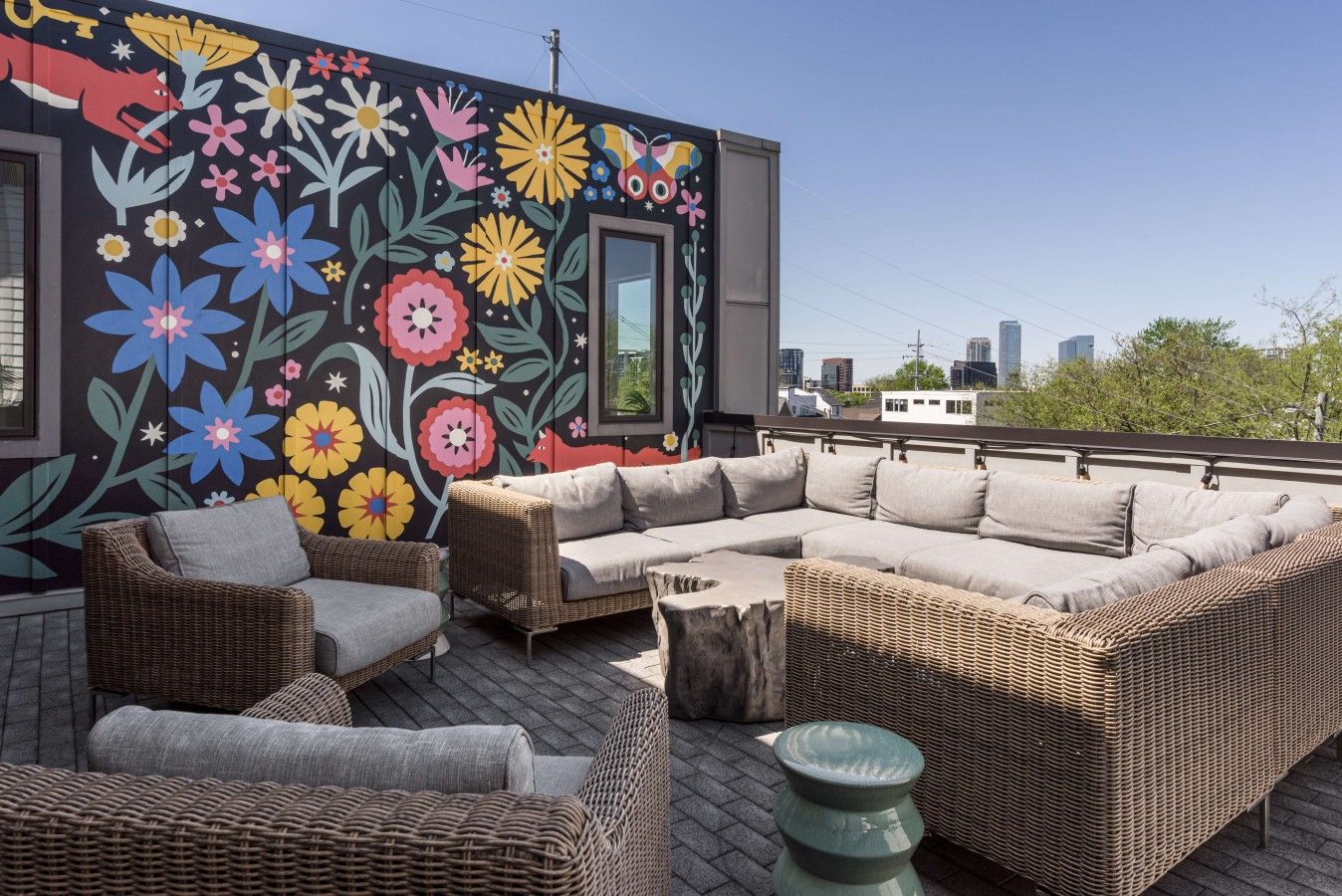 Una terraza en la azotea con mobiliario de mimbre, un mural colorido y vistas de la ciudad.