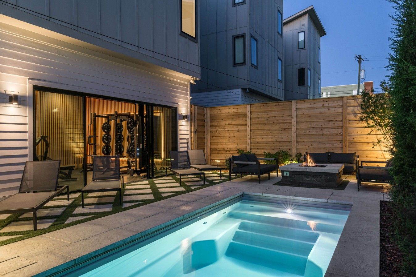 Un espace piscine extérieur moderne, doté d’un jacuzzi intégré, de chaises longues et d’une clôture en bois.