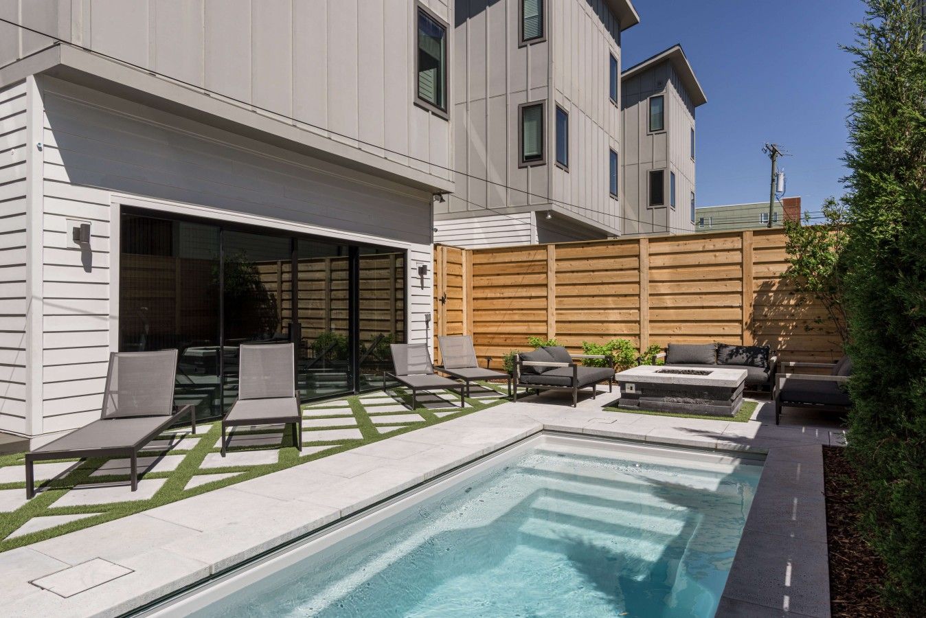 Un área de piscina moderna al aire libre con un jacuzzi integrado, varias sillas de descanso y una valla de madera.