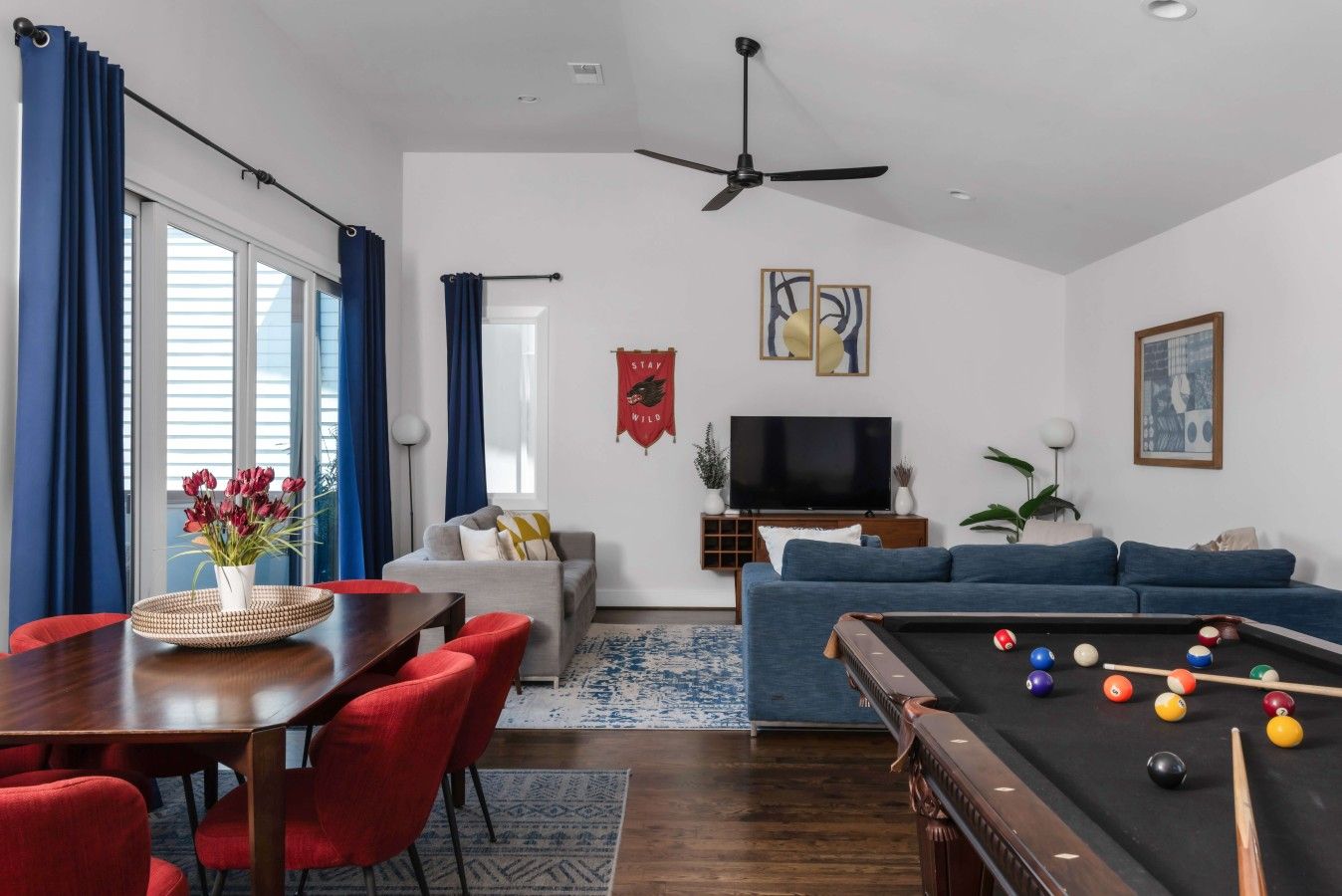 Uma sala de estar com mesa de bilhar, sofá, televisão e um espaço de jantar com cadeiras e mesa.