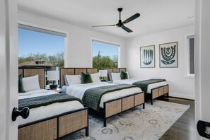 A bedroom with three beds, large windows, ceiling fan, and artwork on the wall. - Sunny Modern Oasis • Pool, Hot Tub, Fire Pit, Grill, Rooftop (Nashville)