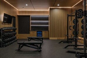 A gym with weightlifting equipment, a television, and a wall-mounted sound system. - Sunny Modern Oasis • Pool, Hot Tub, Fire Pit, Grill, Rooftop (Nashville)