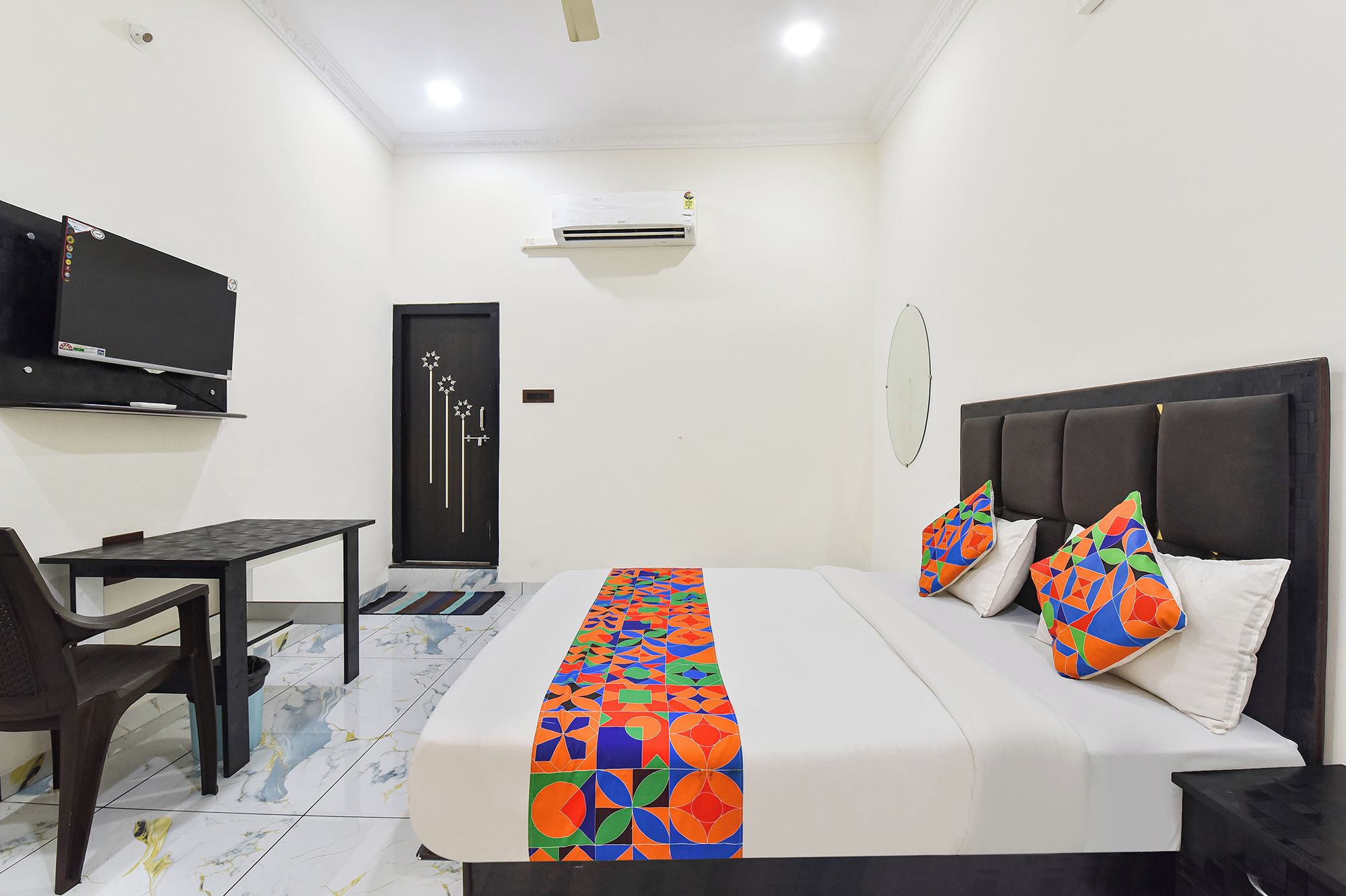 A hotel room with a bed, a desk, a chair, a TV, and an air conditioning unit.