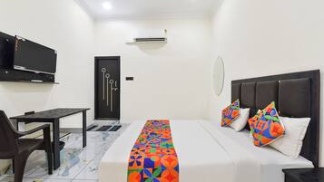 A hotel room with a bed, a desk, a chair, a TV, and an air conditioning unit.