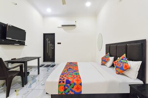 A hotel room with a bed, a desk, a chair, a TV, and an air conditioning unit.