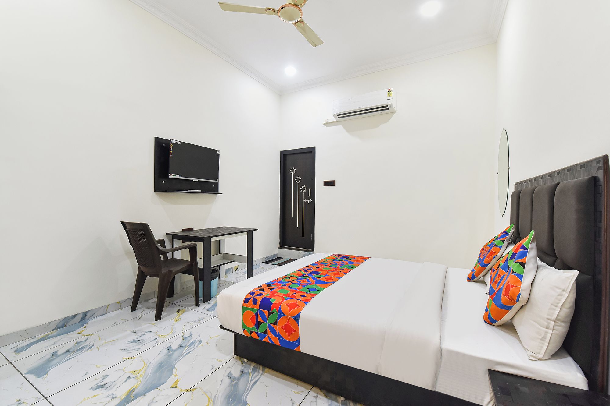 A hotel room with a bed, a desk, a chair, a television, and an air conditioning unit.