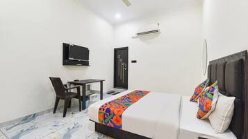 A hotel room with a bed, a desk, a chair, a television, and an air conditioning unit.