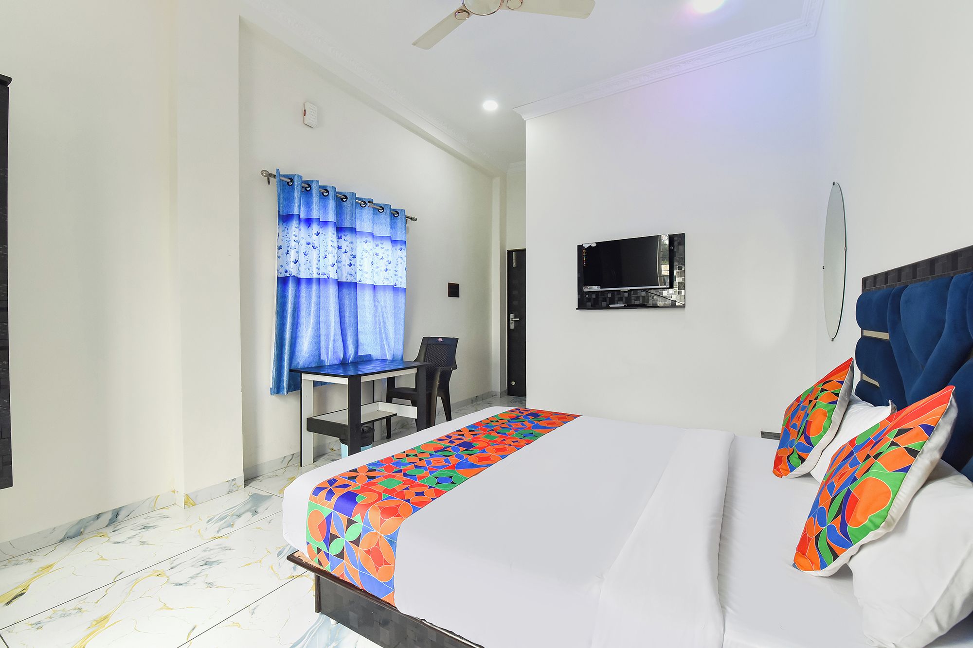 Habitación de hotel con cama, escritorio, silla, televisión y ventilador de techo.