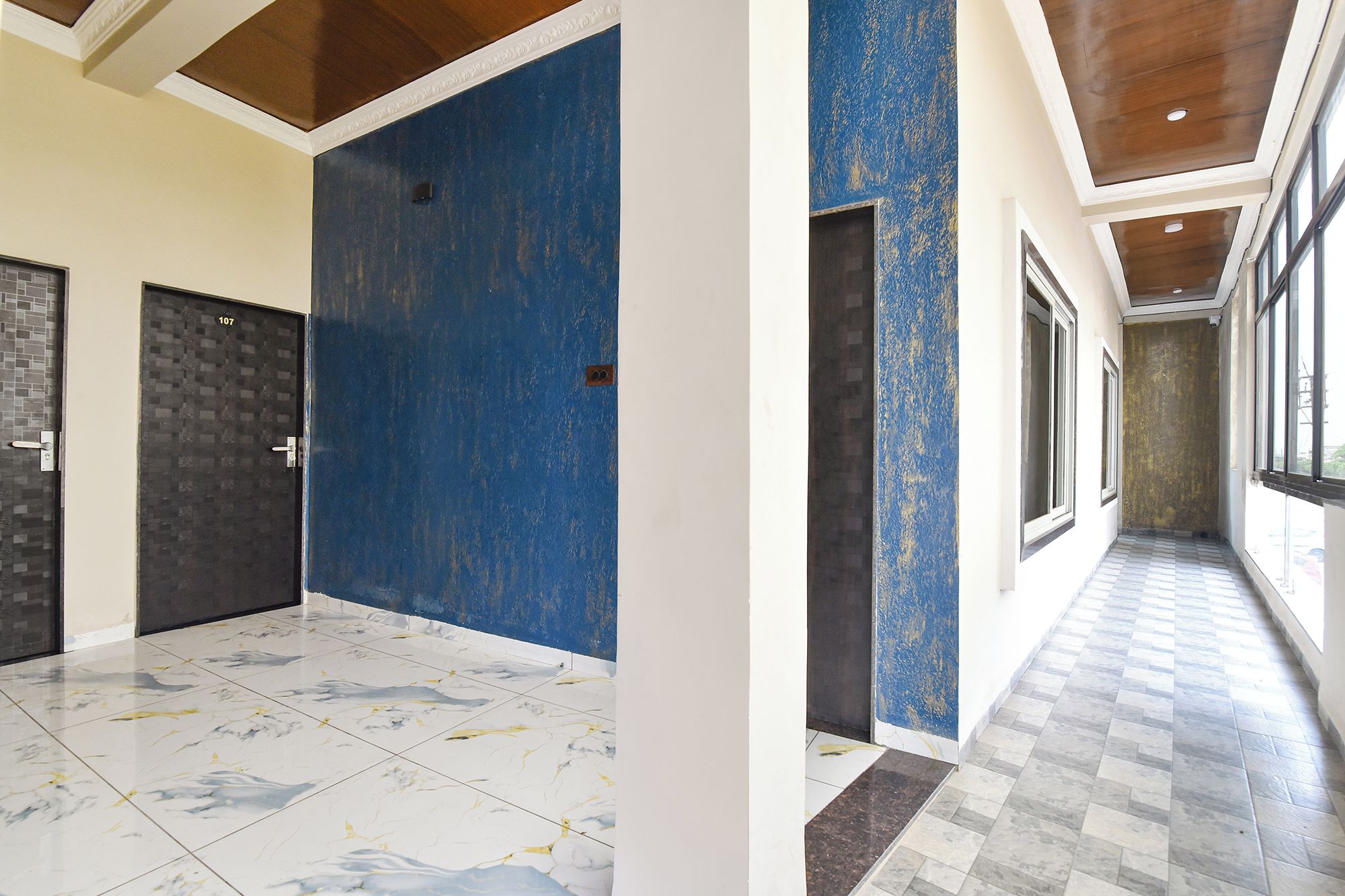 A hallway with a blue door, a tiled floor, and a corridor with windows.