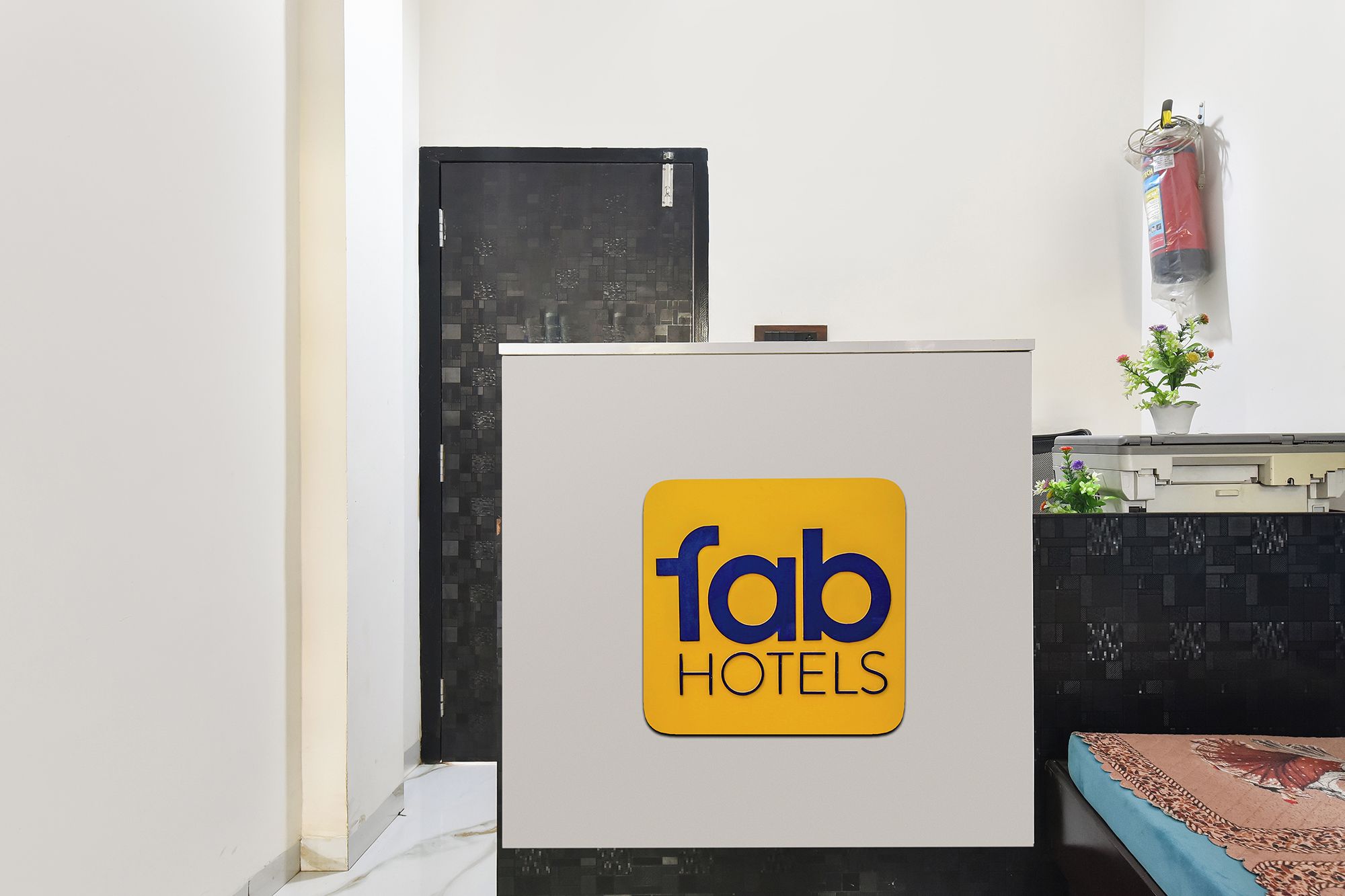 Un comptoir d’accueil avec une enseigne indiquant « fab hotels », une porte noire et une petite plante en pot posée sur le comptoir.