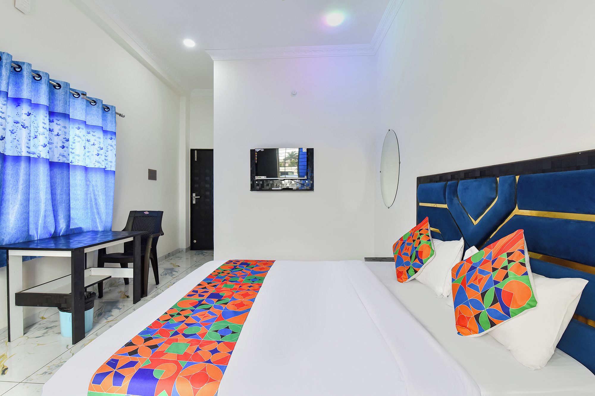 A hotel room with a bed, a desk, a chair, a TV, and a window with curtains.