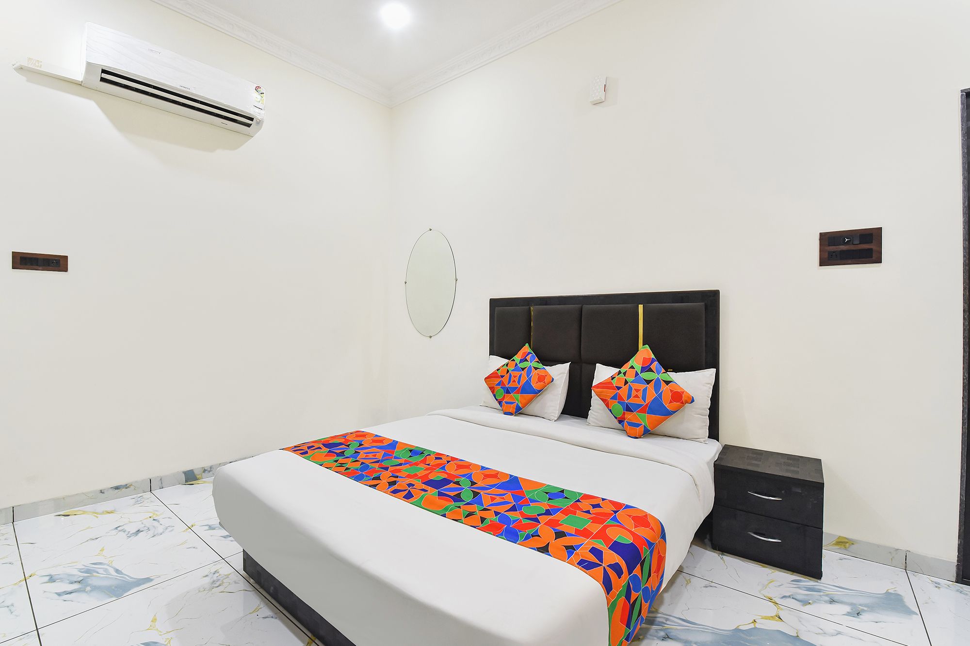 Una habitación de hotel con cama, mesita de noche y un equipo de aire acondicionado.