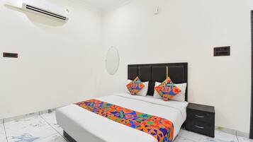 Una habitación de hotel con cama, mesita de noche y un equipo de aire acondicionado.