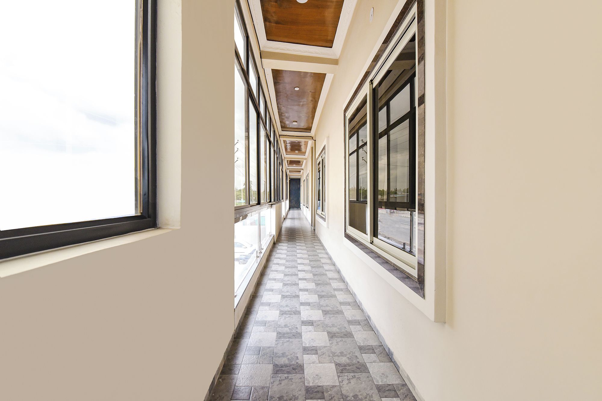 A corridor with large windows on both sides, leading to a door at the end.