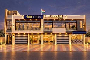 Un hotel moderno con fachada de dos pisos, una bandera y un cartel que indica 'HOTEL CHOICE INN AC ROOMS'.
