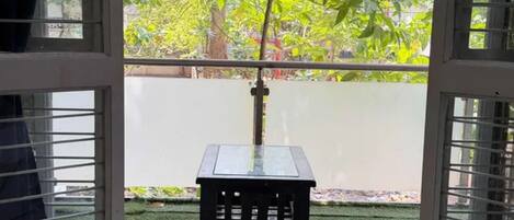Une vue à travers une fenêtre, avec une petite table et de l’herbe artificielle à l’extérieur.