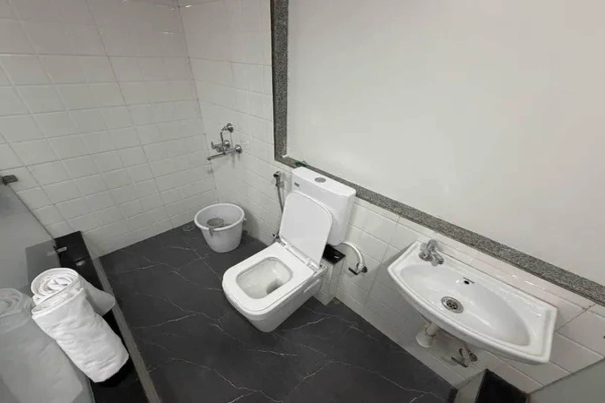 A bathroom with a toilet, a bidet, a sink, and a trash bin.
