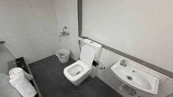 A bathroom with a toilet, a bidet, a sink, and a trash bin.