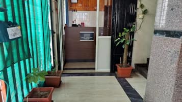 A hotel reception area with a wooden counter, a sign for the hotel, and potted plants.