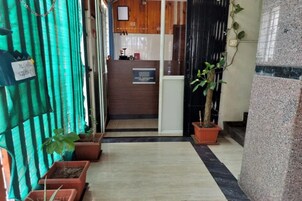 A hotel reception area with a wooden counter, a sign for the hotel, and potted plants.