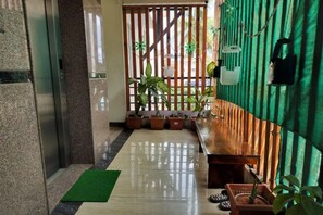 A hotel lobby with a reception desk, potted plants, and a green curtain.