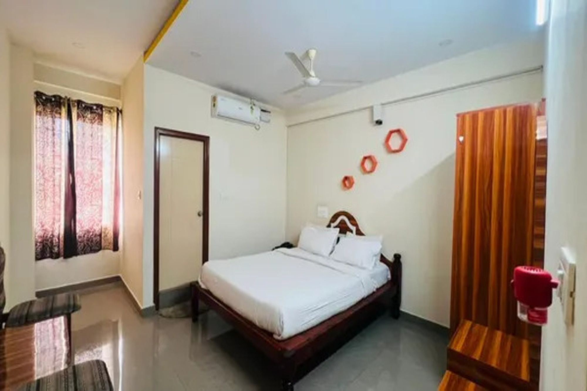 Ein Hotelzimmer mit Bett, Deckenventilator, Tür und einem Fenster mit Vorhängen.