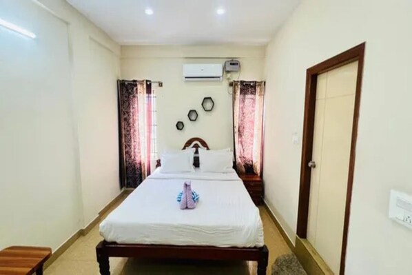 A bedroom with a bed, a door, an air conditioning unit, and a window with curtains.