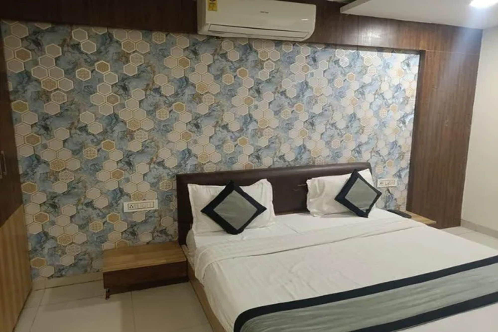 Un dormitorio con cama, cabecero de madera, pared con azulejos de patrón hexagonal y un equipo de aire acondicionado sobre la cama.