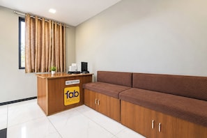 A reception area with a wooden desk, a reception sign, a brown sofa, and a window with curtains. - FabHotel D9 (Indore)