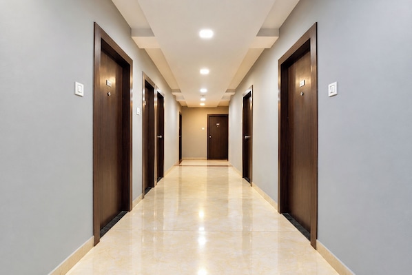 Corredor de hotel com várias portas, piso ladrilhado e iluminação embutida no teto.
