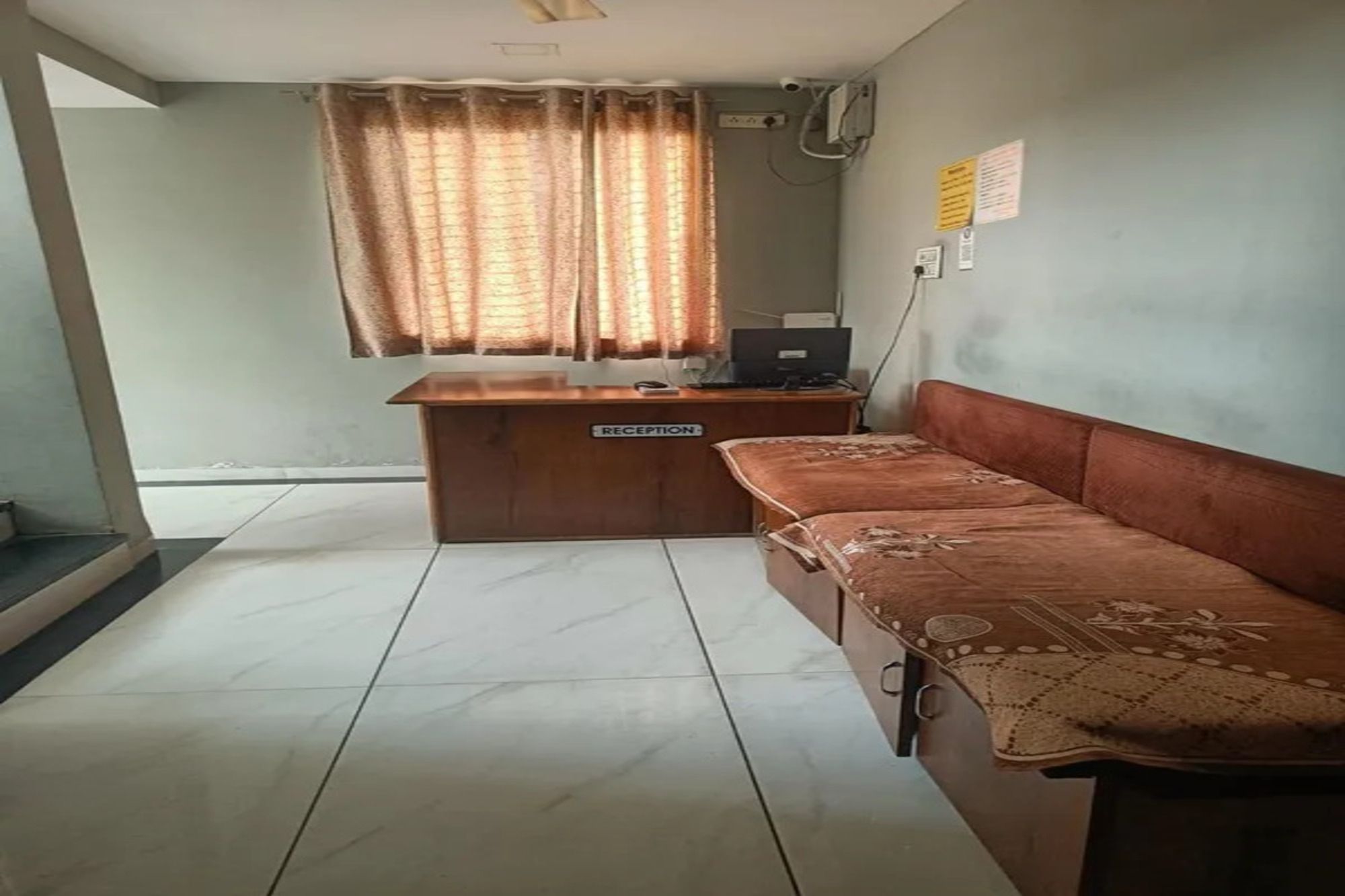 A reception desk with a sign, a sofa, a window with curtains, and a wall-mounted air conditioning unit.